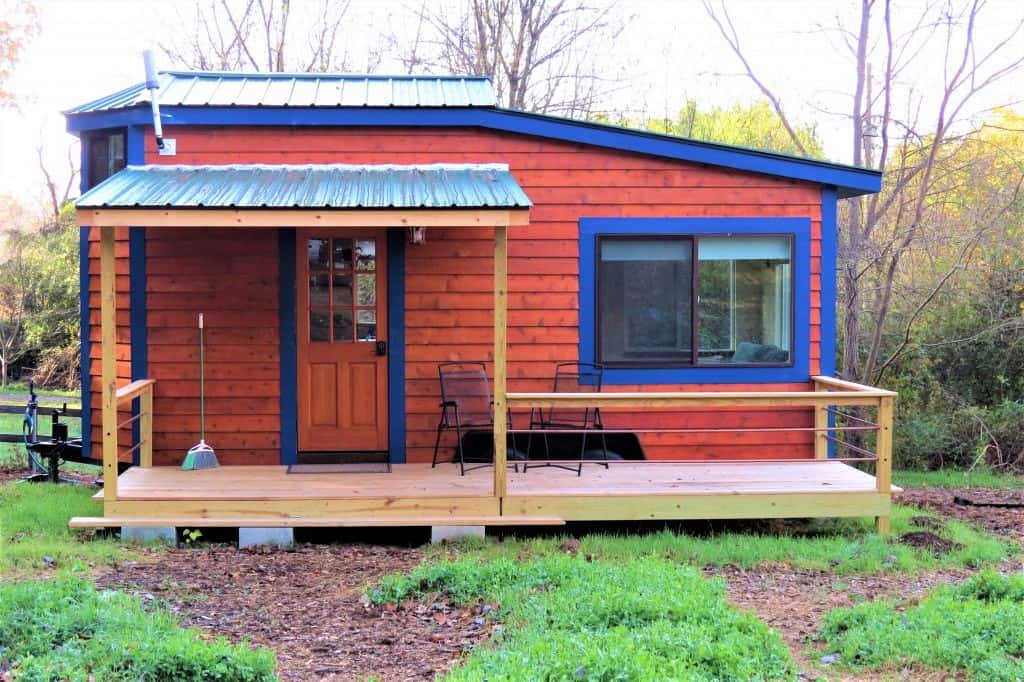 Tiny home with stained wood and blue trim exterior with small unstained porch out front.