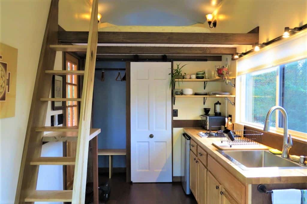 Other side of the tiny home with a full view of the kitchen, storage, and door to bathroom.