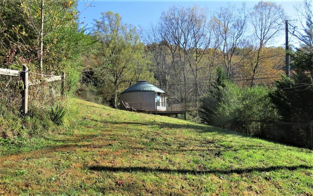 Yurt in a field with porch wrapping around two-thirds.