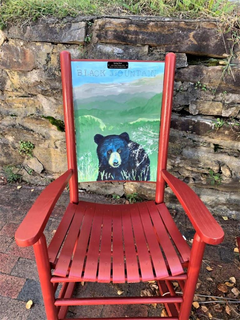 Red rocking chair with hand painted photo of a bear on the street in Black Mountain, NC.