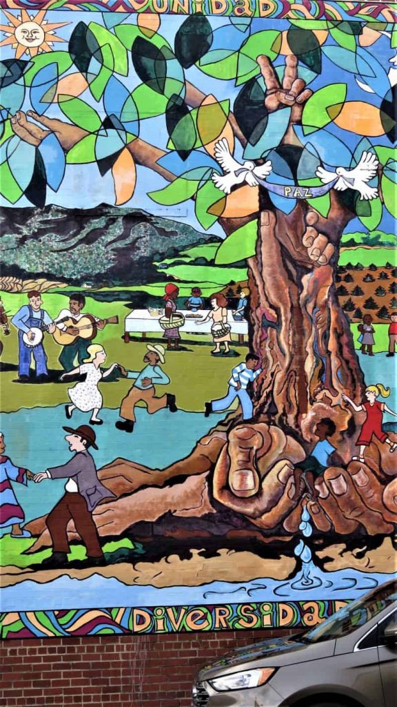 Street mural of a tree with colored leaves and people having a picnic and dancing