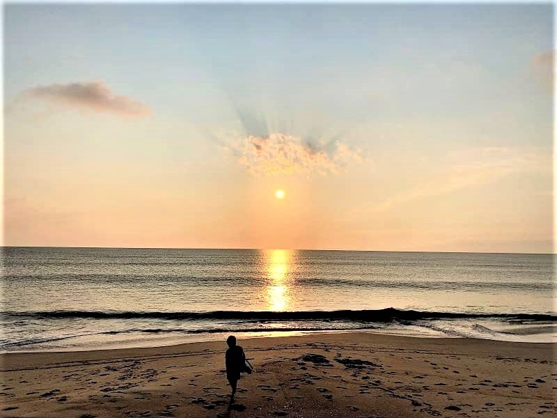 Sunrise at the beach with only one child on the sand.
