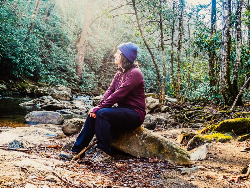 Woman sitting on rock by Jacob Fork River in the morning.