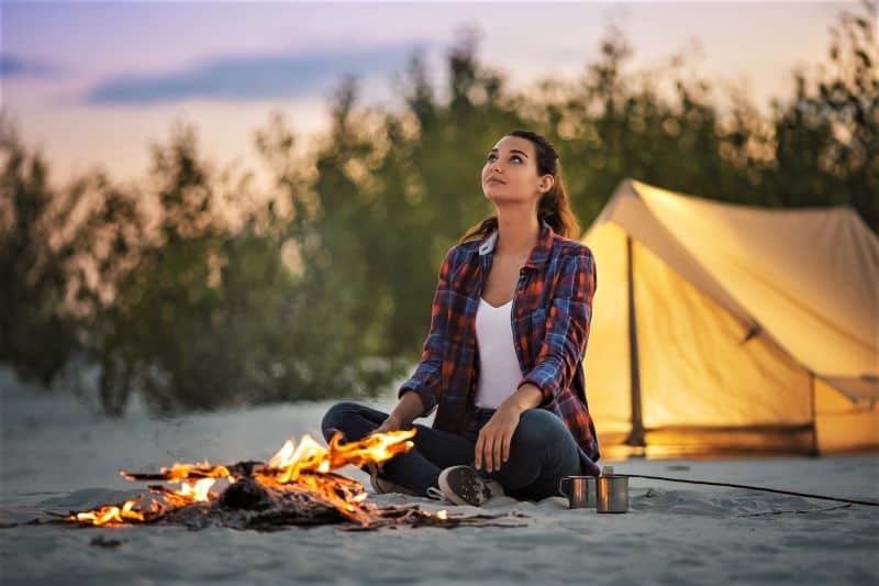 Woman camping alone sitting by a fire.