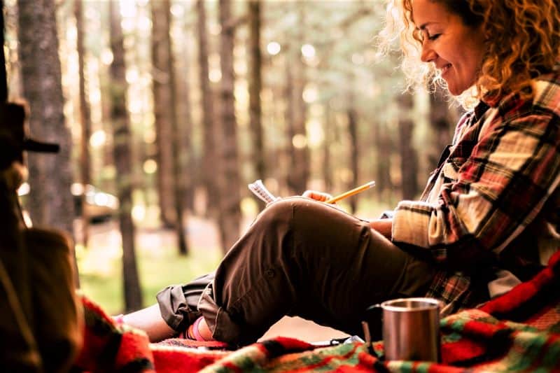 Woman at camp, writing in a small notebook.