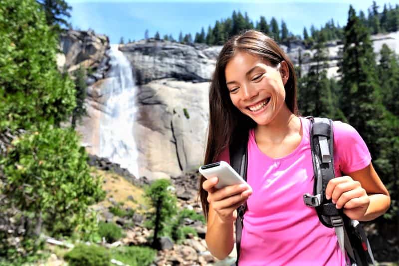 Woman hiking near waterfall checking phone.