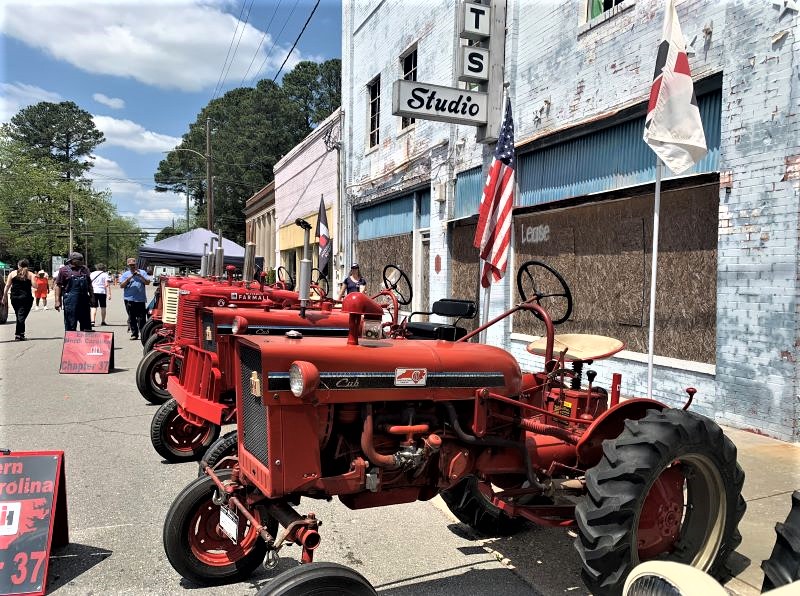 Row of red vintage tractors along the street at the Pickle Festival.