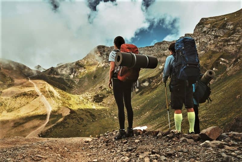 Two backpackers standing on a mountain, one has a heavy backpack.