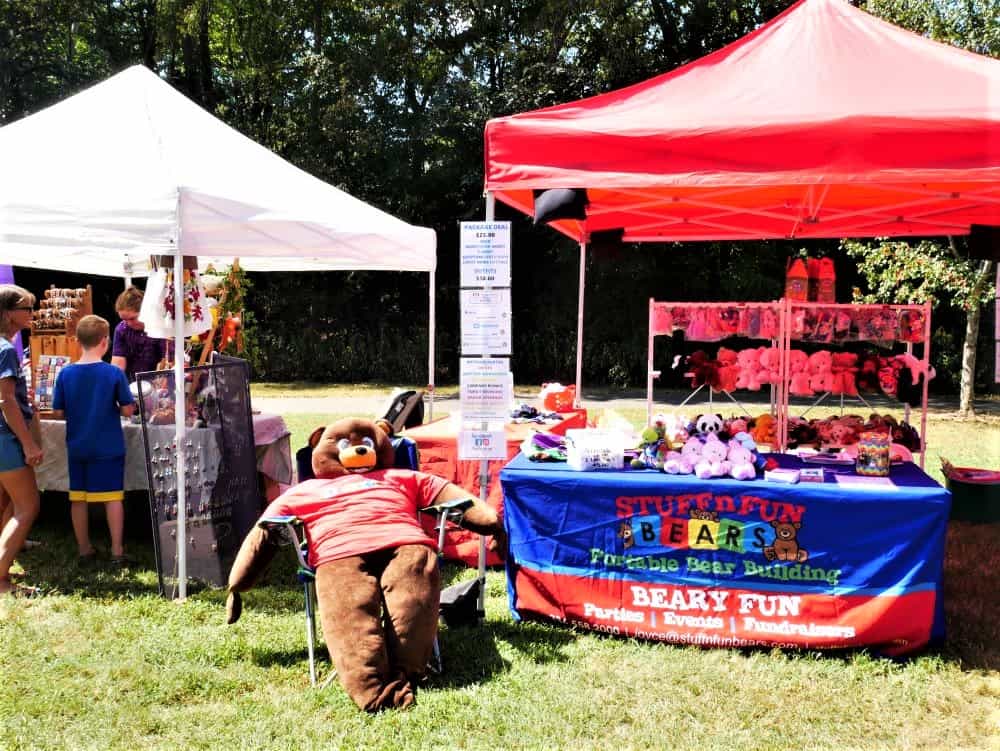Large stuffed bear in chair by vendor booth at Hog Day Festival