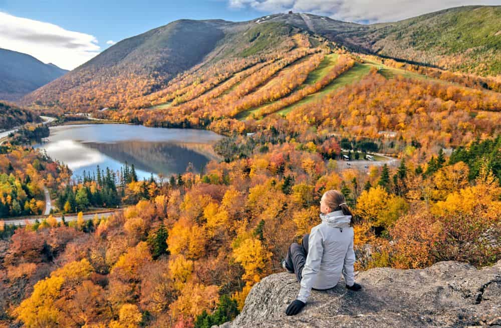 Woman sitting on overlook viewing fall trees below.