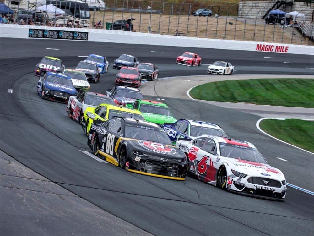 Several stock cars rounding a turn in a NASCAR race.