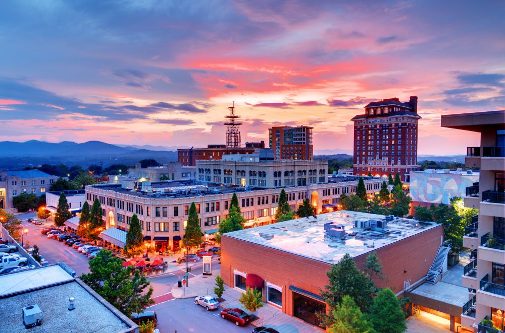 Aerial view of downtown Asheville at night with pink sky in the background.