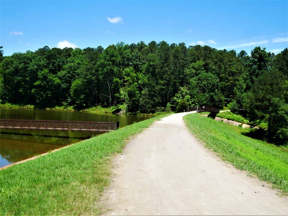 Trail passing by pier and bridge by lake at Umstead State Park.