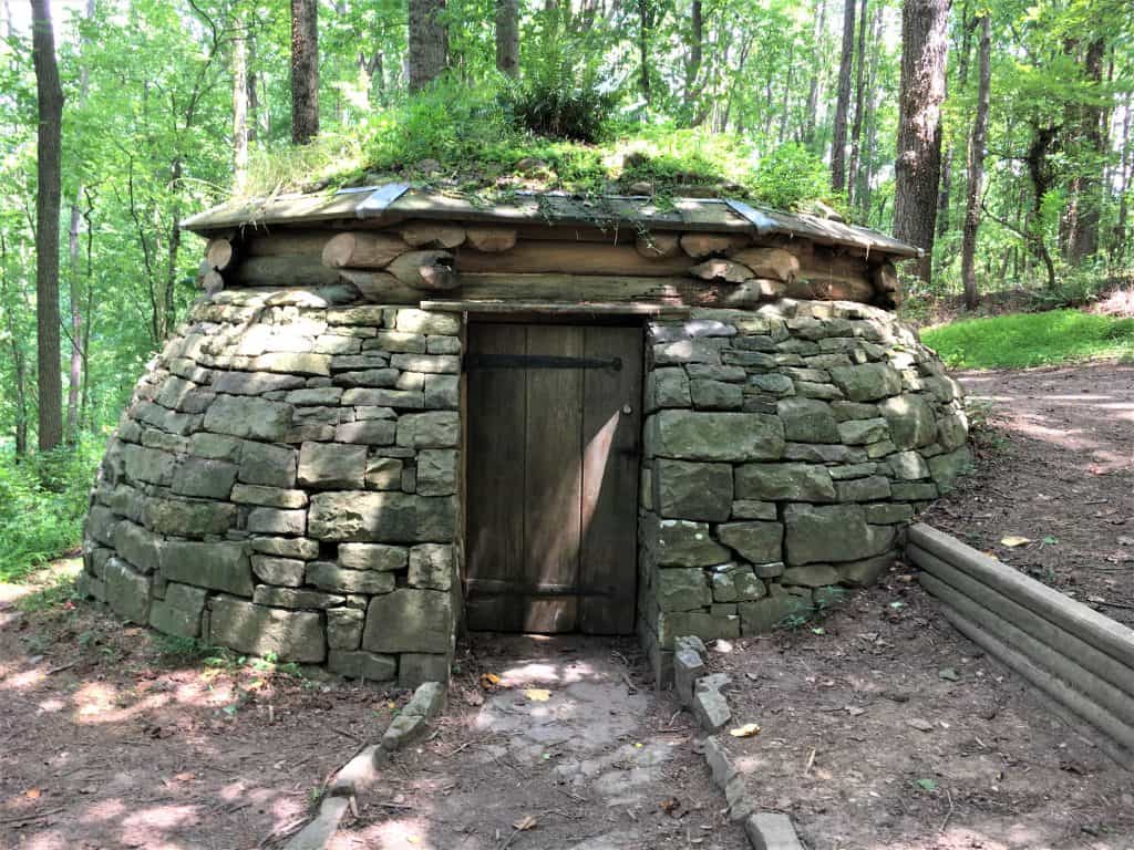 A round, stone house with grass growing on the roof. There is a small wooden door. 