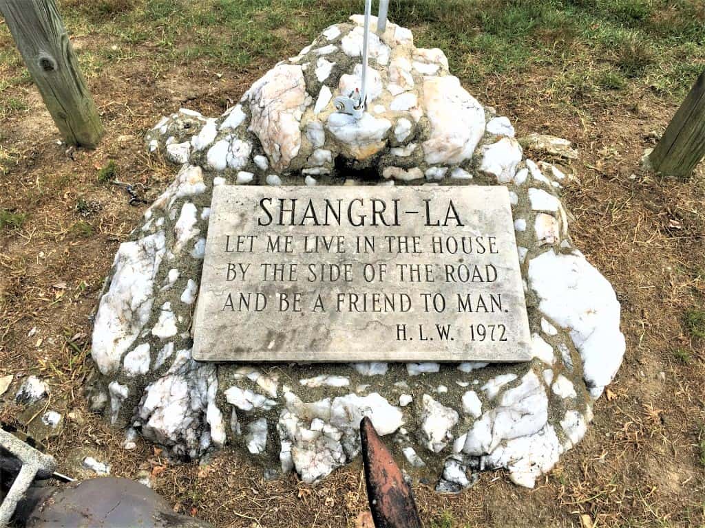 A group of stones with a plague on top that says "Shangri-La. Let me live in the house by the side of the road and be a friend to man. H.L.W. 1972". 