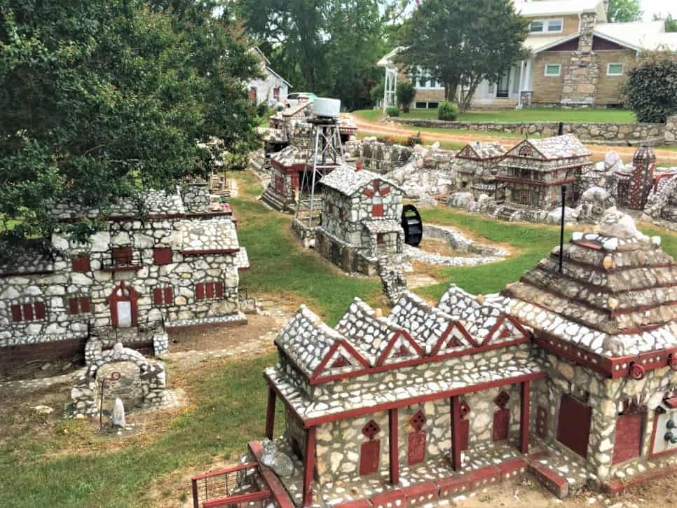 A small village in a side yard made of red and white stones. There is a water tower, church, and over 10 additional buildings. 