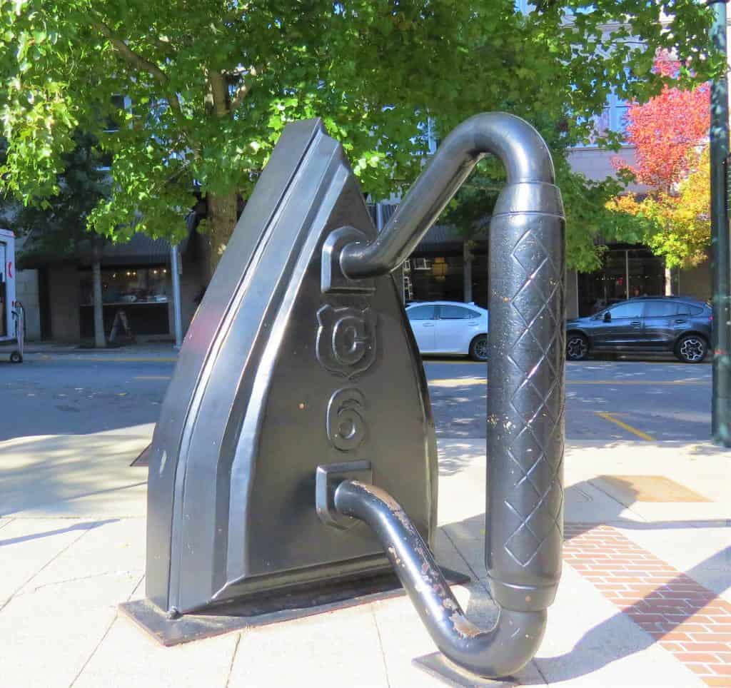 A large sculpture of an iron that is taller than a human on a street. 