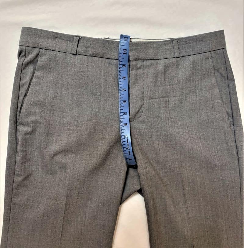Grey hiking pants laying flat with a blue tape measure showing the distance from the waistband to the crotch.