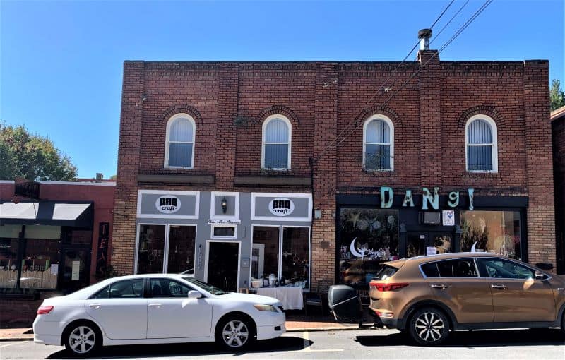 Stores on a street in downtown Black Mountain. There is a single story brick building on the left attached to a large two story brick building split into two businesses.  The first is a beer store and the second has a blue sign that says, "Dang!". 