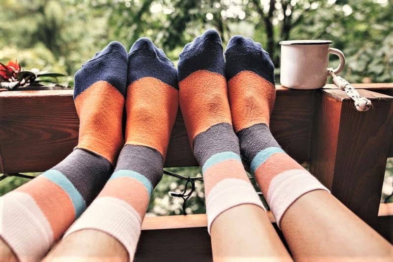 Two sets of legs with feet propped on porch fence. Both are wearing the same striped socks that are various shades of blue and orange.