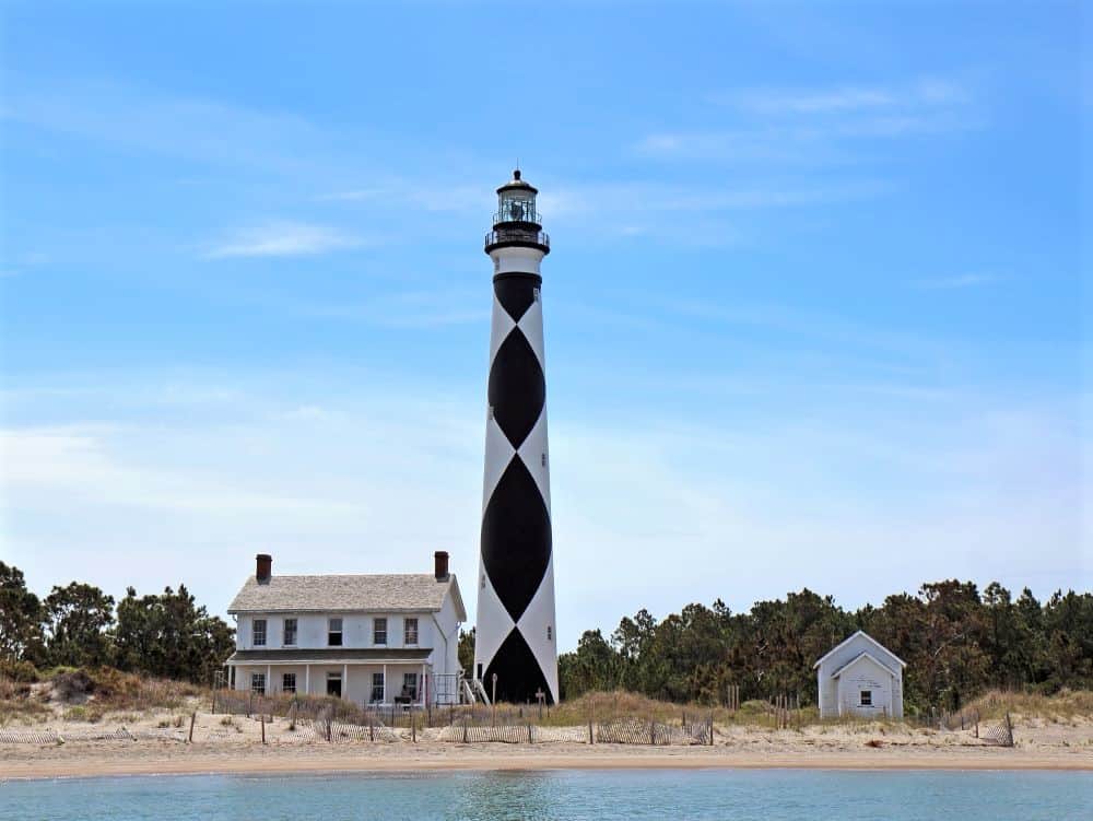 Cape Lookout lighthouse with black and white diamond pattern and white house next to it. 