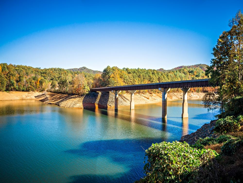 A bridge going over Fontana Lake with trees on either side and bright blue water and sky. 