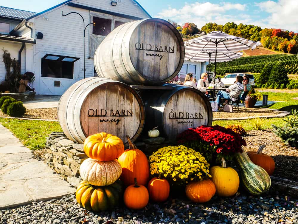 Three barrels in a pyramid that say "old Barn Winery) with assorted gourds in front of them for decoration.