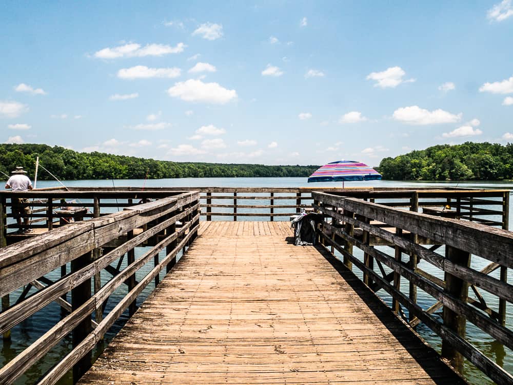 Fishing pier in shape of a T with pink and blue sun umbrella and man fishing.