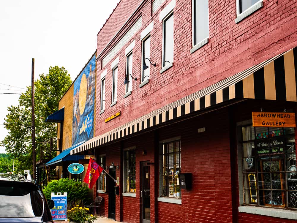 Red two story brick building with yellow and black striped awning and sign for Arrowhead Gallery.