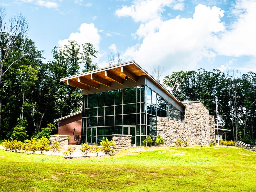 Building with glass wall in front and stone on the side in a green field. 