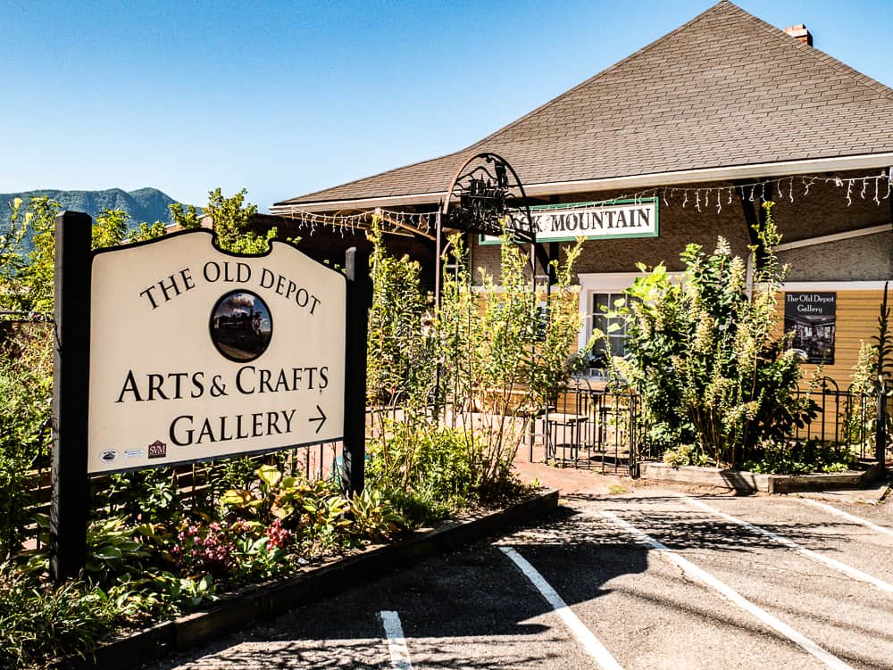 Photo of sign for the Old Depot Arts and Crafts Gallery with the yellow building behind it. 