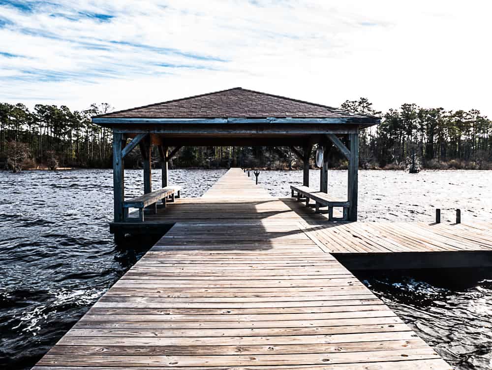 Wooden boardwalk with covered area in the middle over a rough lake that is kicked up by winds.
