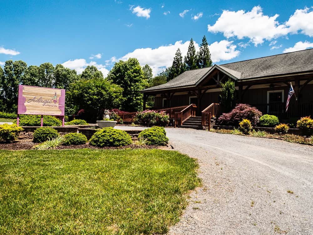 Brown building with a gravel circle drive and wooden sign out front noting Adagio tasting room. 