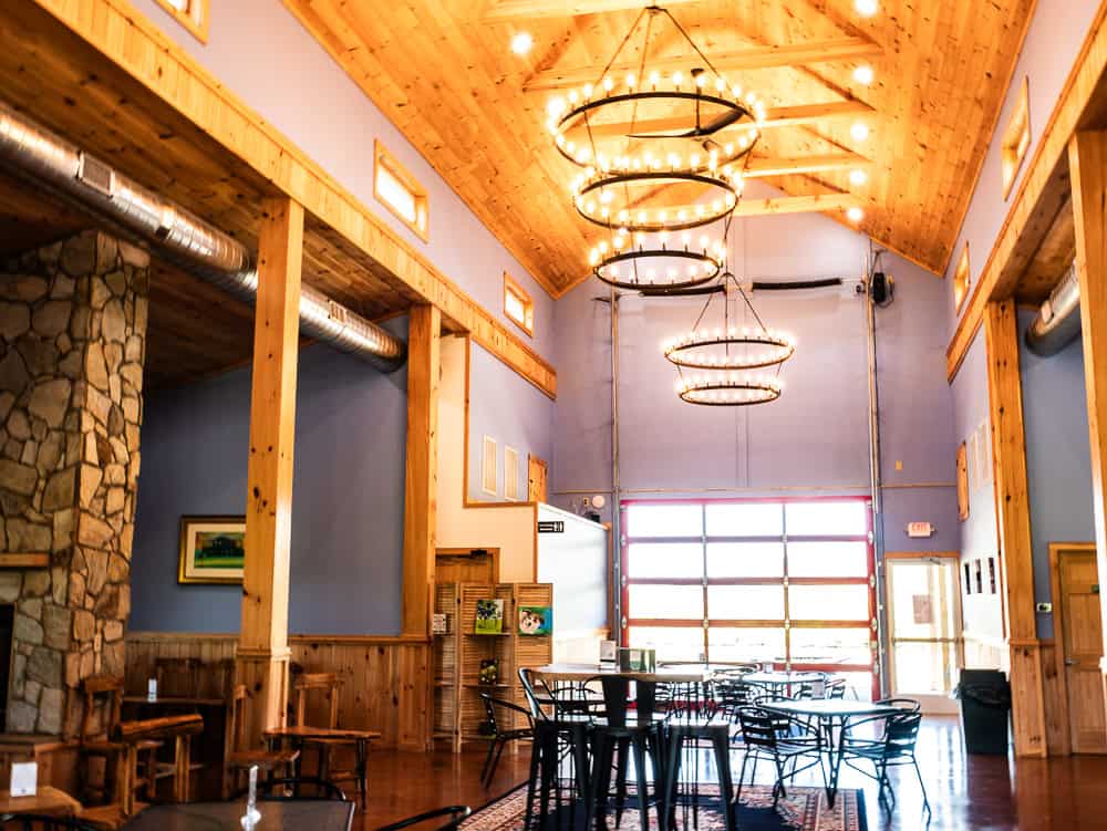 Renovated barn with high ceilings and large chandeliers over tables. The walls are painted blue and there is a stone fireplace to the left. 