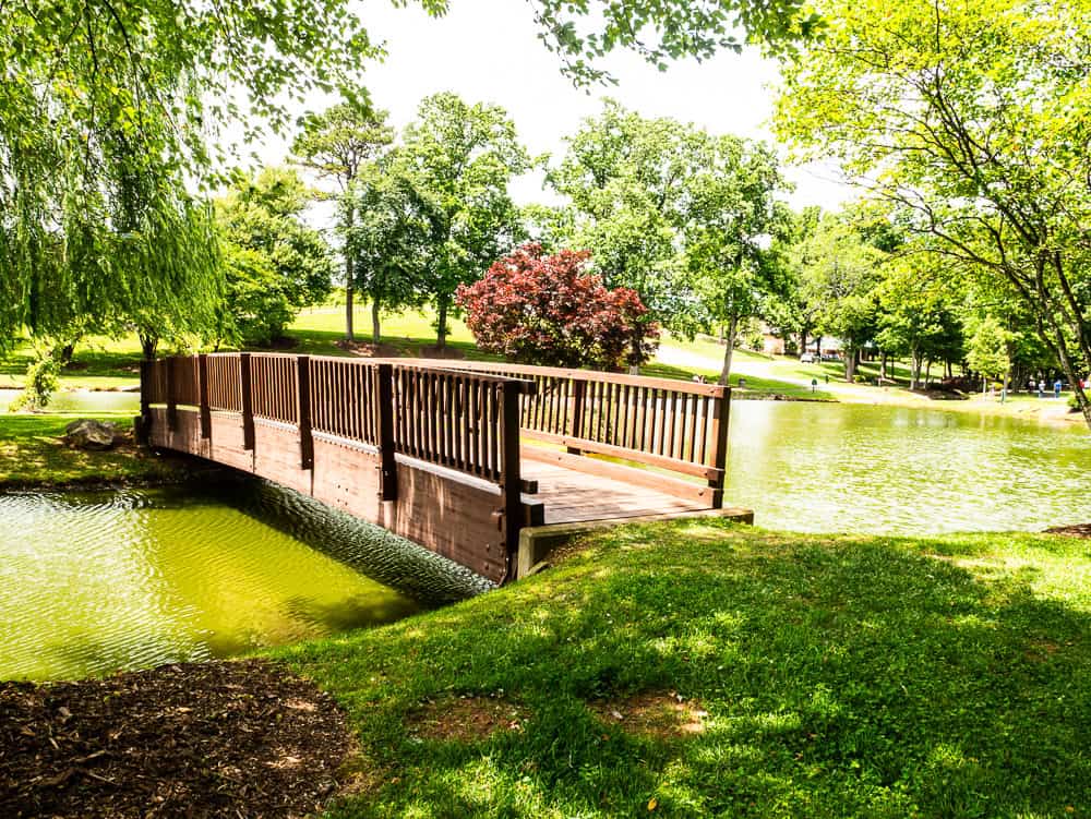 A wooden bridge crosses over a narrow section of a small pond to an island. 