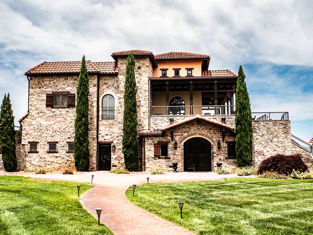 Brown stone two story Tuscan Style villa with a black door and balcony on the second floor. 