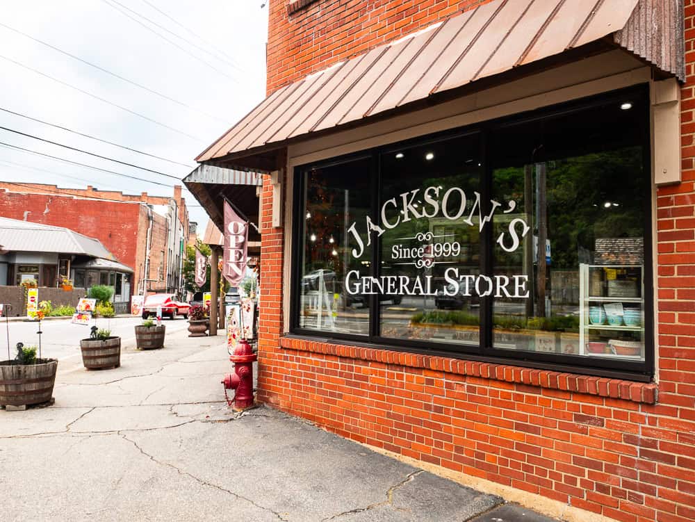 Old red brick building with large window that has Jackson's General Store since 1999 on the window. The street curves and there are other brick buildings in the background. 