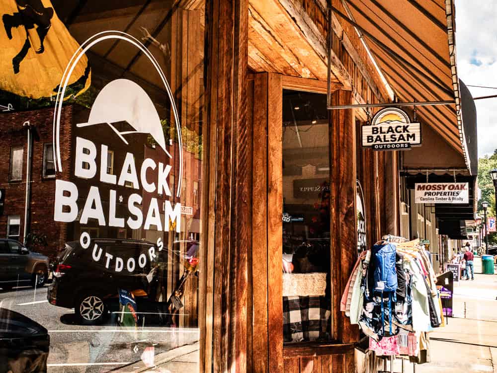 Wooden building with clothes on a rack out front. White signage on the window shows a tent and the words Black Balsam Outdoors. 