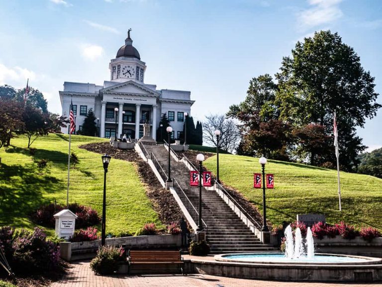 White two story building up a steep hill with a staircase leading to it. There is a fountain at the bottom of the staircase. The building looks similar to the Whitehouse and has a clock tower on the top.