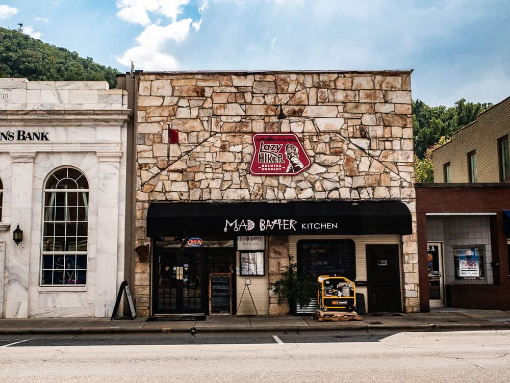 A building with a brown stone façade with a red sign noting Lazy Hiker Brewing Company and a black awning for Mad Batter Kitchen. 